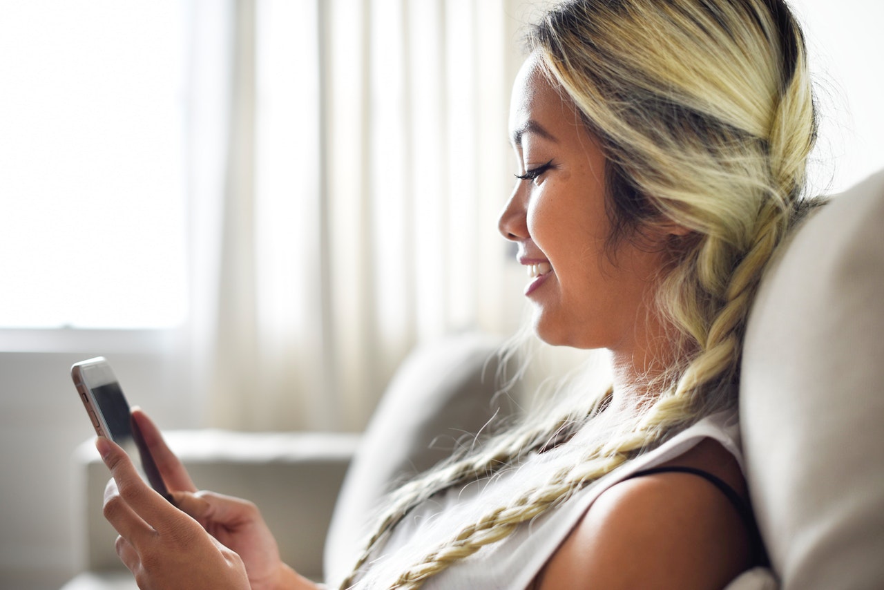 Close-up Photo of Smiling Woman Sitting on Sofa Using Smartphone